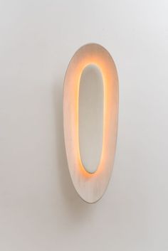 a white wall mounted light with an oval shaped light on it's side,