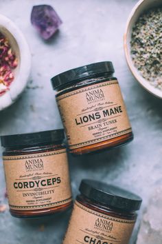 three jars of honey sitting on top of a table next to bowls of dried herbs