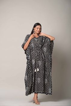 Pattern - Kaftan with dori & white Tassels Colour - Black background with gray and white print Print - Hand Block Printed Sleeves - 3/4th loose sleeves Neck design - V- neck Wash - Hand Washable Dress length - 52 inch Fabric - 100% Cotton Our Hand Block Print Blue Kaftan comes in a big and bold indigenous print with a delicate border design. The airy silhouette of the Kaftan gives you maximum comfort and makes this a very breathable attire. It features three-quarter sleeves. This easy-wearing Kaftan is perfect for any occasion, but you can also use it as a loungewear. Bohemian Kurta With Tassels For Navratri, Traditional Festival Kurta With Tassels, Bohemian Tassel Dresses For Navratri, White Festive Dresses With Tassels, Festive White Dress With Tassels, Festive White Dresses With Tassels, Bohemian Kurta With Tassels For Eid, Bohemian Tasseled Kurta For Eid, Traditional Kaftan With Back Tassel Tie-up For Festivals