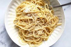 a white bowl filled with pasta covered in parmesan cheese on top of a marble counter