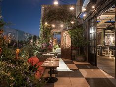 an outdoor dining area is lit up with hanging lights and potted plants on the patio