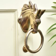 a metal horse head mounted to the side of a white door with a ring on it