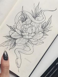 a woman's hand holding a pencil and drawing flowers on a book with an snake wrapped around it