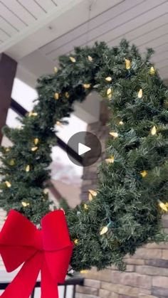 a christmas wreath on the front porch with red ribbon and lights hanging from it's side