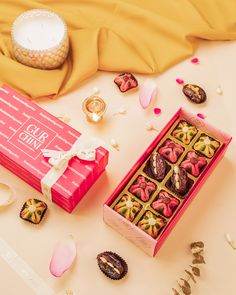 a pink box filled with assorted chocolates next to a candle and other decorations