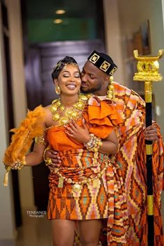 a man and woman dressed in traditional african garb hugging each other while posing for the camera