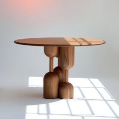 a round table with three wooden legs in front of a white wall and light coming through the window