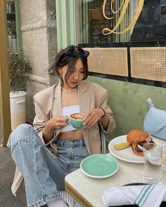 a woman sitting at a table with food in front of her and eating from a bowl