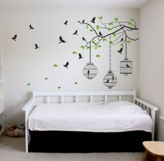 a white bed sitting under a tree with birdcages on it's branches