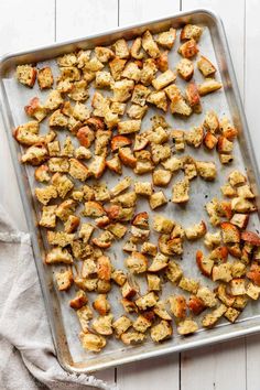 a pan filled with chicken and potatoes on top of a wooden table next to a towel