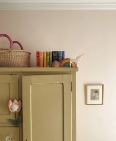 a bookcase with books and a basket on top of it in a room that has pink walls