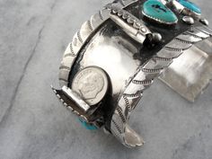 This is a watch band cuff bracelet, intended for a gentleman, and made in the American Southwest at some time around 1970 or so. The style is interesting, a slightly off set motif that allows the watch to be fully visible without turning the wrist. These turquoise nuggets are lovely, bright blue with wonderful deep silver matrix. Metal: Sterling Silver Gem: 4 Turquoise Nuggets Gem Measurements: Size and Shape Varies Width: 1 1/1 Inches Inside Diameter: 2 1/2 Inches Southwestern Turquoise Cuff Bracelet, Southwestern Style Turquoise Cuff Bracelet With Inlay, Southwestern Blue Cuff Jewelry, Southwestern Style Blue Nickel-free Cuff Bracelet, Bohemian Turquoise Nickel-free Cuff Bracelet, Cuff Watch, Native American Turquoise, American Turquoise, A Gentleman