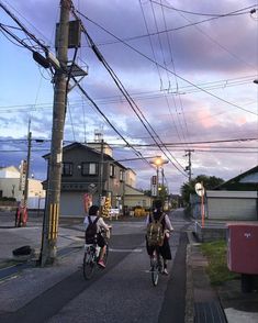 two people riding bikes down the street in front of power lines and telephone poles at dusk