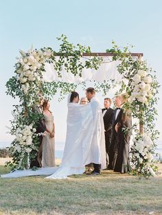 a bride and groom standing under an arch with white flowers on it at their wedding ceremony