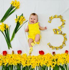 a baby is laying in the middle of some flowers and letters that spell it's 3