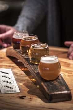 five glasses of beer are lined up on a wooden table with a sign that says,