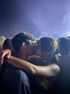 two people kissing each other while standing in front of a crowd at a music concert