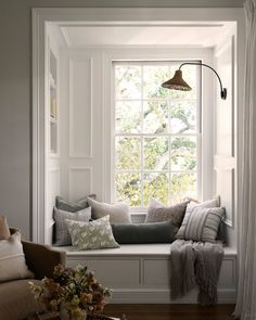 a window seat with pillows on it in front of a window sill and a lamp