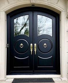 a black double door with two sidelights and gold handles in front of a house