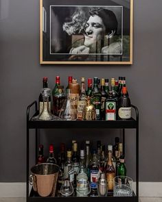 a bar cart filled with liquor bottles next to a painting