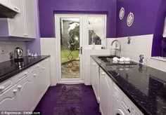 a purple kitchen with white cabinets and black counter tops is seen in this image from the front door