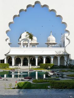 an ornate white building with many windows and arches on the roof is reflected in a pool surrounded by greenery