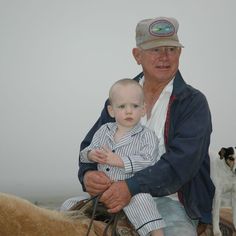 an older man sitting on top of a horse holding a baby