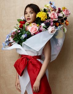 a woman in a red and white dress holding a bunch of flowers on her shoulder