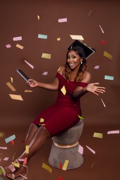 a woman in a graduation cap and gown sitting on a stool surrounded by confetti