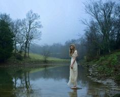 a woman is standing in the middle of a body of water on a foggy day