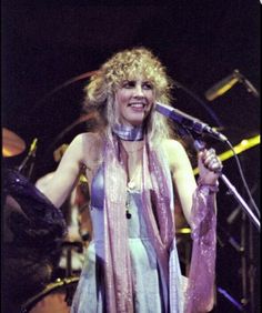 a woman standing in front of a microphone and holding a scarf around her neck with both hands