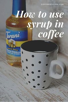 a coffee cup sitting on top of a wooden table next to a bottle of syrup