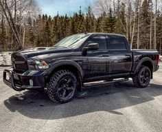 a black ram truck parked in a parking lot next to some trees and snow covered ground