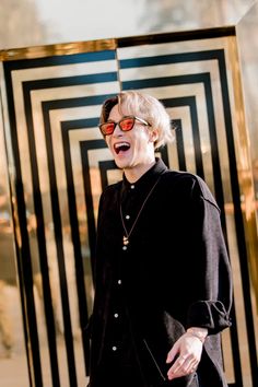 an older woman wearing sunglasses standing in front of a black and white striped wall