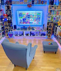 two chairs and a couch in front of a large screen tv on a wall with shelves full of toys