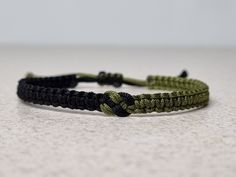 a green and black bracelet on a white counter top, with one knot in the middle