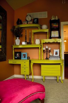 a yellow desk with pink ottoman and mirror on the wall in a room that has orange walls