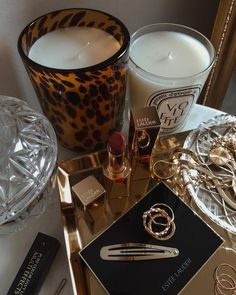 a table topped with candles and jewelry next to a glass container filled with lipstick on top of it