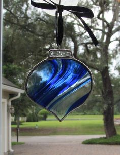 a blue and white ornament hanging from a glass window with trees in the background