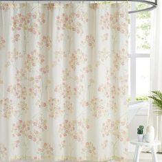 a shower curtain with pink flowers on it in front of a white wall and window