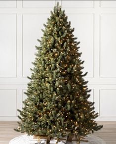 a christmas tree with lights on it in front of a white wall and wooden floor