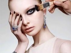 a woman with makeup brushes her eyes while she is getting ready to brush her nails