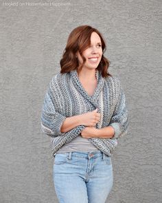 a woman standing in front of a gray wall with her arms crossed and smiling at the camera