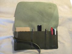 A simple and efficient way to store and keep organized your favourite pens, pencils, and stationery products. Grab a small notebook (moleskine or Field Notes will fit), a couple pens and you're on your way. Want to access an item, simply unroll the case. When you are done, simply roll the case back up and secure with the buckle. If properly cared for, this pen roll should last you a lifetime. --Materials-- Seaweed Green top grain 3-4 oz 99% veg tan leather and nickel plated rivet, nickel plated Green Organizers With Pen Holders For Daily Use, Green Organizer With Pen Holders For Daily Use, Daily Use Green Organizer With Pen Holders, Functional Everyday Organizer With Pen Slots, Green Travel Stationery With Pen Holders, Green Pencil Case With Pen Slots, Functional Everyday Organizers With Pen Holders, Modern Organizers With Pen Holders For Daily Use, Modern Travel Organizers With Pen Holders