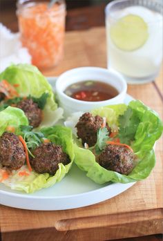 meatballs in lettuce with carrots and sauce on a plate next to a glass of water