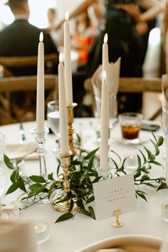 the table is set with candles, greenery and place settings for an elegant dinner