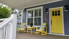 two yellow chairs on the front porch of a blue and white house with yellow doors