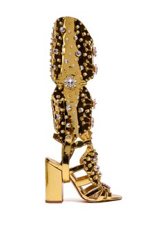 Knock ‘em dead in The AZALEA WANG Norinne Gold Embellished Gladiator Open Toe Sandal Boot. This ultra-luxe convertible style features a patent faux leather upper, an open almond toe silhouette, a chunky high heel, a tonal cushioned footbed, faux gold metallic hardware, a wide frontal footband, and a cage-like, strappy cut out appearance. For a multifunctional design, this metallic pair has an easily detachable, rounded knee-high shaft with strappy buckle detailing, elasticized back panels, cut out accents, decorative layered paneling, and a snap button strap that loops under the heel, allowing for quick removal. Complete with a dazzling sea of assorted gem and rhinestone embellishments, circular studded detailing, pave rhinestone pendants, a pull-on fit, and an adjustable buckled ankle str Gold Leather Heels With Rhinestones, Gold Leather Sandals With Rhinestones, Embellished Gold Leather Sandals, Gold Embellished Leather Sandals, Gold Studded Heels For Party, Luxury Gold Heels With Rhinestones, Gold Sandals With Round Toe And Gold Studs, Club Heels, Knee High Gladiator Sandals