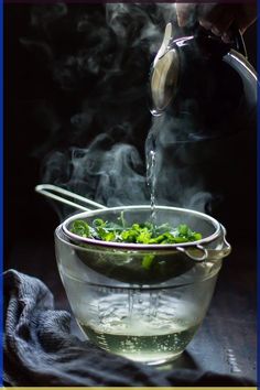 a person pouring water into a glass bowl filled with green vegetables and steam rising from it