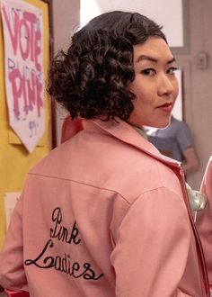 a woman with curly hair wearing a pink hoodie and looking off to the side